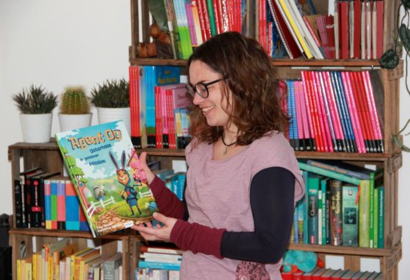 Kinderbuchautorin Katharina Mauder präsentiert eines ihrer Bilderbücher vor Regal voller Kinderbücher